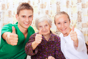 two caregivers and senior woman doing thumbs up